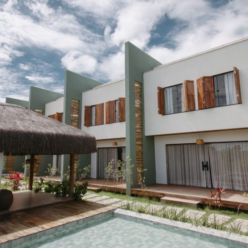 Home Stylish modern villas with wooden accents and thatched roofing by a pool under a vibrant sky in Bahia, Brazil.